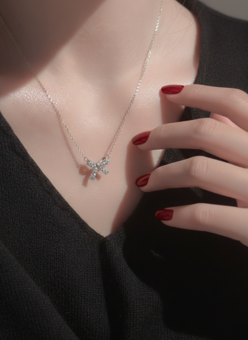 Model wearing a dainty 925 sterling silver bow pendant necklace with sparkling zircon stones, styled with red nails and black V-neck top.