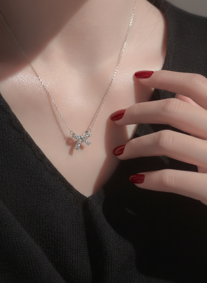 Model wearing a dainty 925 sterling silver bow pendant necklace with sparkling zircon stones, styled with red nails and black V-neck top.