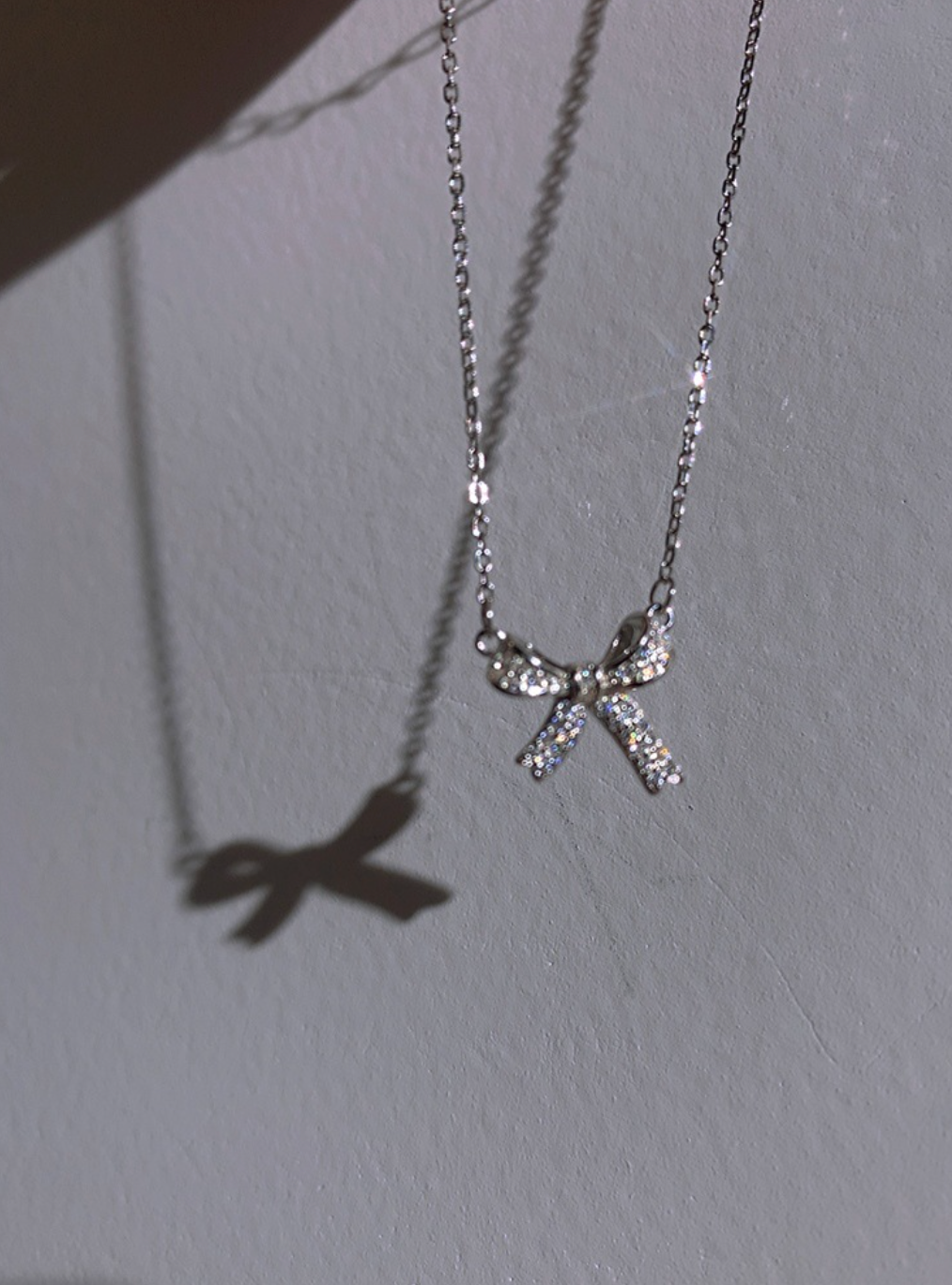 “Sterling silver ribbon bow necklace with sparkling zircon stones and rhodium-plated finish hanging from a delicate link chain.”