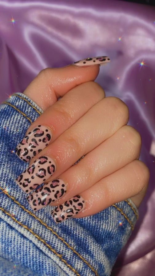 Trendy leopard print press-on nails on a hand against a vibrant purple fabric background.