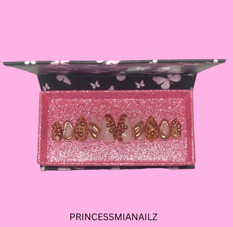 Elegant gold-tone butterfly press-on nails displayed in a sparkly pink jewelry box with a black butterfly pattern lid.