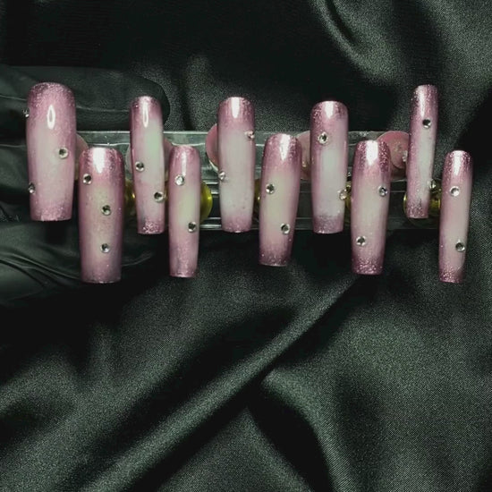 Elegant press-on nails with a regal, shimmering pink finish, displayed on a lush green background for a luxurious, princess-worthy aesthetic.