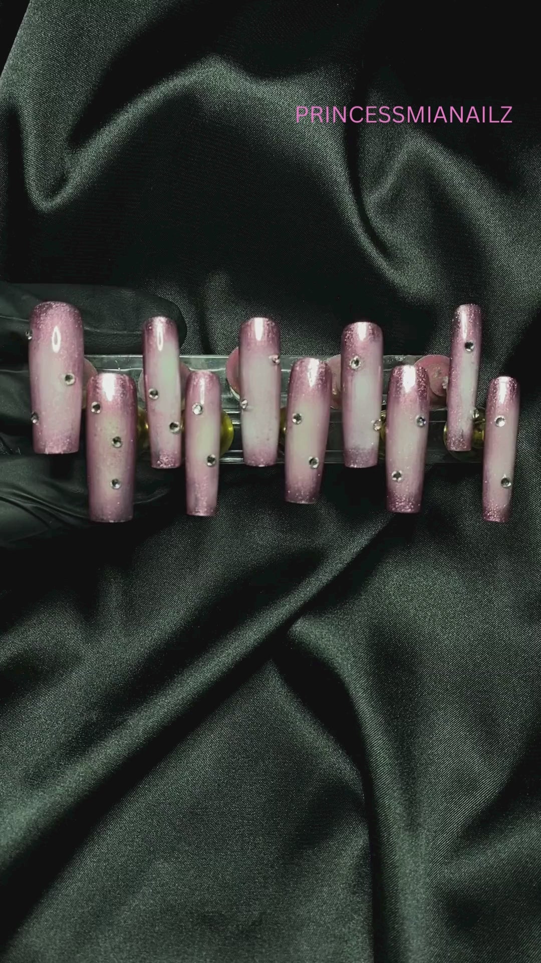 Elegant press-on nails with a regal, shimmering pink finish, displayed on a lush green background for a luxurious, princess-worthy aesthetic.